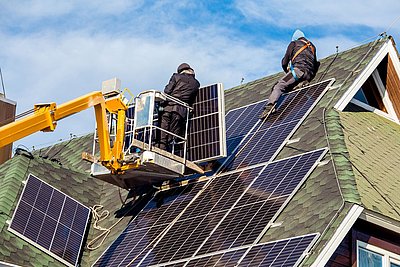 Montagearbeiten auf einem Hausdach: 2 Personen bringen Photovoltaik-Module an
