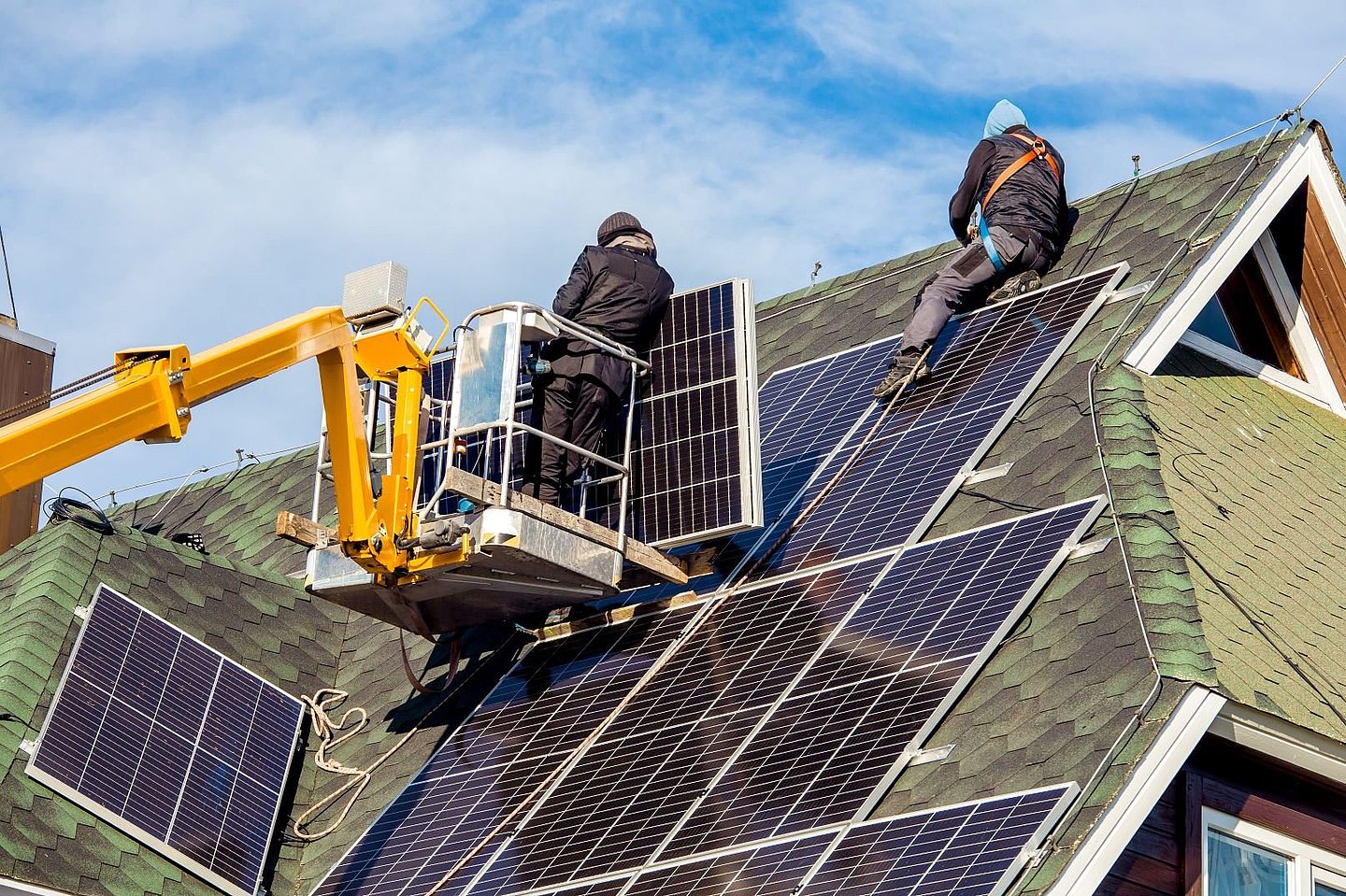 Montagearbeiten auf einem Hausdach: 2 Personen bringen Photovoltaik-Module an
