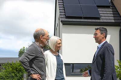 Drei Personen im Gespräch, im Hintergrund ein Haus mit PV-Dachanlage
